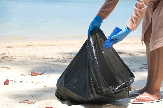 A young woman picks up trash, water bottles, plastic bottles and tons of dirt on the beach. global warming concept
