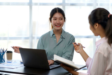 Obraz premium Smiling young Asian businesswomen talking to colleague and exchanging ideas together at office.