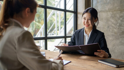 Fototapeta premium Smiling young Asian businesswomen talking to colleague and exchanging ideas together at office.