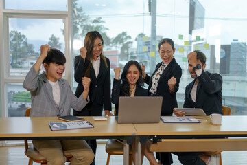 Happy group of young Asian business people successful excited raised hands rejoicing with laptop computer in office. New startup project concept.