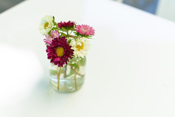 Frasco con flores rosadas, aislado en mesa blanca. Ambiente de verano.