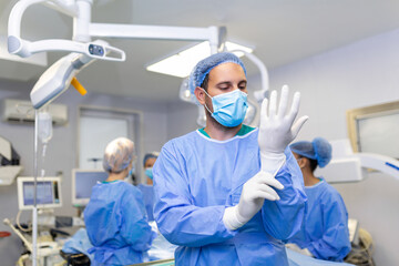 Portrait of male doctor surgeon putting on medical gloves standing in operation room. Surgeon at modern operating room