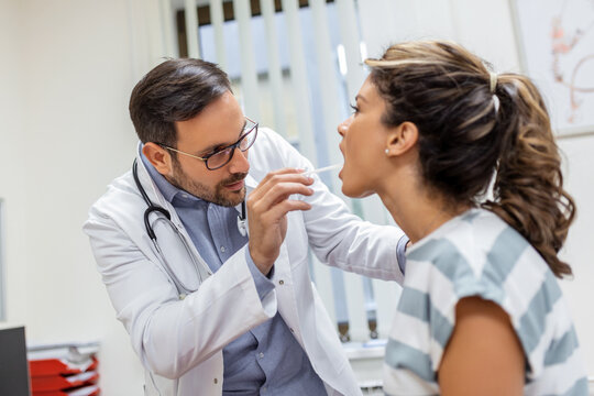 Doctor using inspection spatula to examine patient throat. ENT doctor doing throat exam of a woman. patient opened her mouth to throat check-up