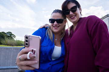 Two plus size girlfriends with sunglasses and hugging to take a selfie smiling together outdoors. Inclusive and diversity concept. Copy space.