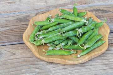 Closeup shot of fresh green peas with seed pods in the plate with wooden background