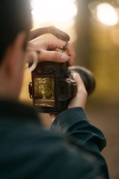 Close up of a man holding a modern photo camera while looking at the screen. Close up of camera using with the screen visible. Concept of an amateur taking photos in the forest.