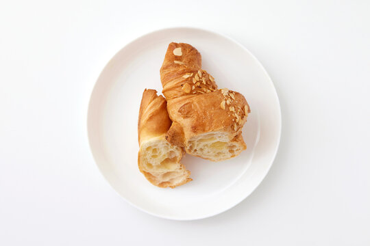 Top view image of sliced french croissant with peanuts served at plate isolated at white background.