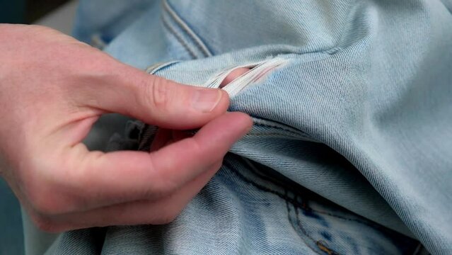 tailor checks the holes rubbed between the legs on women's jeans before darning them. close-up of hands exploring the holes on jeans. the concept of clothing repair or waste recycling.