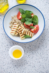 White plate with quinoa, haloumi cheese, spinach and tomato salad, elevated view on a beige granite background, vertical shot