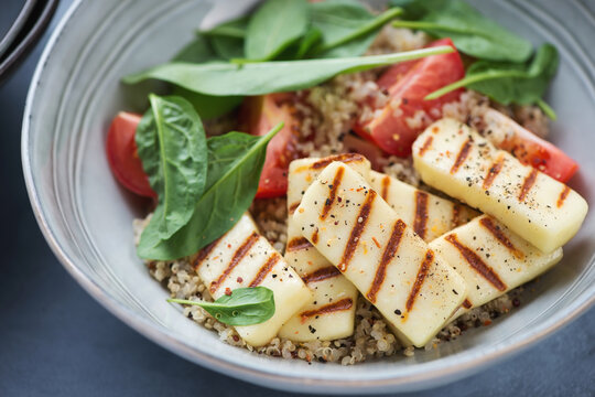 Quinoa with grilled halloumi cheese, fresh spinach and red tomatoes served in a grey bowl, closeup, selective focus