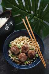 Bowl of ramen noodles with fried meatballs in miso broth, vertical shot with a tropical leaf in the background