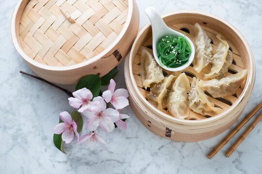 Bamboo steamer with dumplings and seaweed salad on a light-grey marble background, horizontal shot