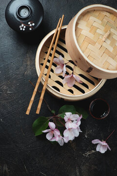 Bamboo steamer and an apple tree branch over dark-brown stone background, vertical shot, above view