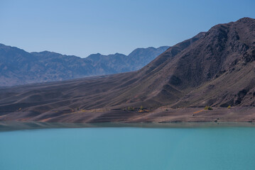 A turquoise lake in the middle of a lifeless valley with mountains in a blue haze in the distance. Gray, dull mountains with a bright lake.