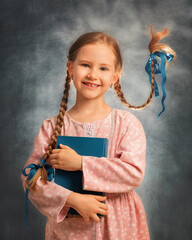 Close portrait of a happy girl kid with two flying braids on a gray background with book