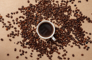 Naklejka premium Cup of coffee with coffee beans on paper background. Top view