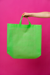 Female hand holding eco or reusable shopping bag against pink background