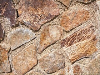 Background photo of rust brown rustic stone wall texture with cement seam.
stones placed diagonally.