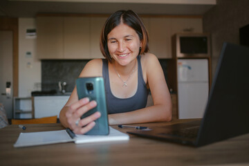 Busy young woman talking on smart phone with clients, coworkers, working remotely on laptop in morning. Female freelancer tutor student having phone conversation call.