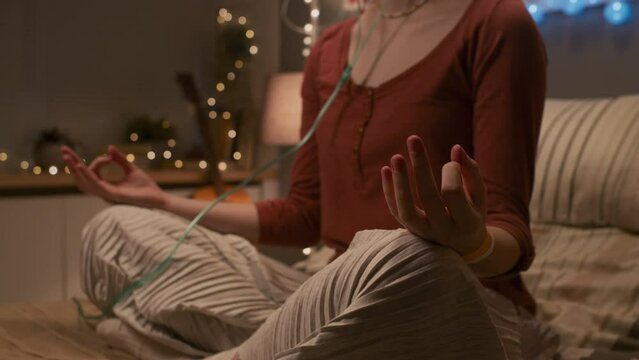 Tilting down of short-haired teenage girl with nasal cannula sitting on bed in hospital room, meditating