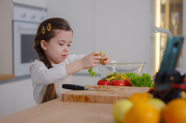 Young Girl Vlogger Making Social Media Video About Cooking At Home, looking on smartphone on tripod. episode about healthy eating. concept of attraction children to healthy diet of early age