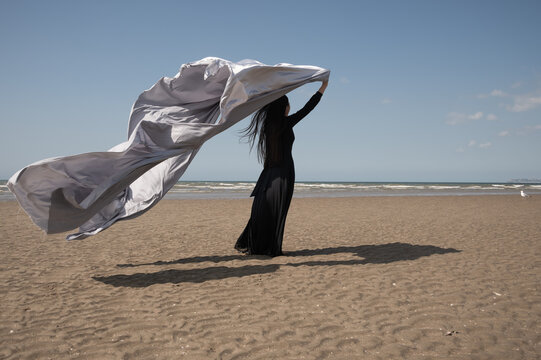 woman in black dress on the beach with silver fabric in the wind