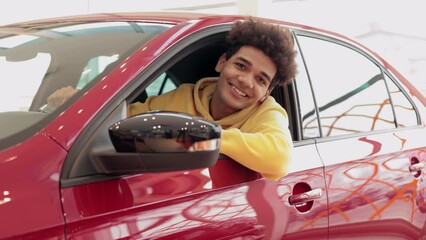 Portrait of young man is testing new transport and posing for camera in modern company spbi. Closeup view of handsome caucasian guy sits inside car and looks with smile, poses in good mood and makes