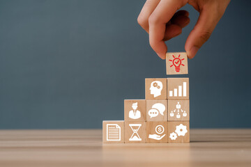 Hand puts the wooden cubes with light bulb on hand icon on beuatiful grey background and copy...