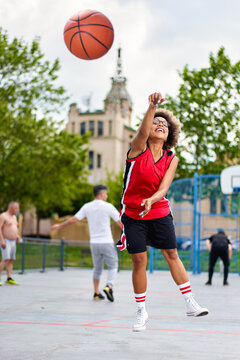 Basketball Player Performing Slam Dunk On A Street Court. Woman In Sportswear Playing Streetball On Summer Day