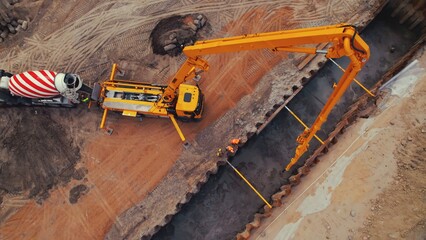 Wide drone shot of a tall yellow crane and a tanker lorry during works at a road construction site pouring cement over a foundation. High quality photo © PoppyPix