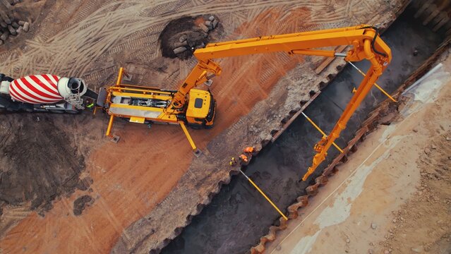 Wide Drone Shot Of A Tall Yellow Crane And A Tanker Lorry During Works At A Road Construction Site Pouring Cement Over A Foundation. High Quality Photo