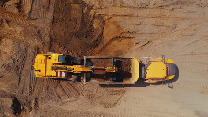 Aerial view of a yellow digger and a tipper truck. Digger loading piles of sand into the tipper....