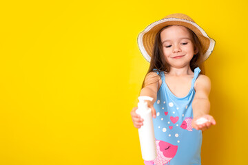 Sun protection. A little girl in a swimsuit and hat uses sunscreen. Yellow background, space for...