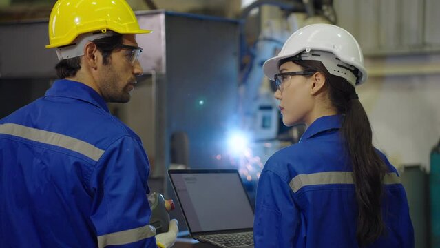 Industrial engineer using laptop computer checking and control automation steel welding robot arms machine, Robotics and manufacturing concepts