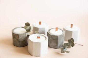 Handmade candles from paraffin and soy wax in concrete plaster candlestick with wooden wick and dry herbal isolated on pastel beige background. Copy space