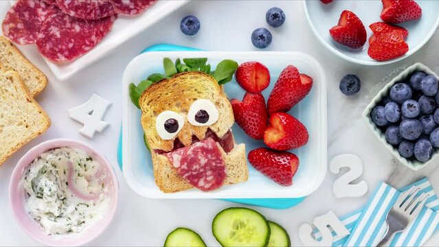 Making school lunch box with a fun salami monster sandwich and fresh berries - strawberries and blueberries. Stop motion animation