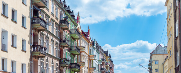 Perspective view on tenements in Nysa, Poland on a summer, sunny day. Ornamental facades with decorative windows and balconies against blue, cloudy sky.