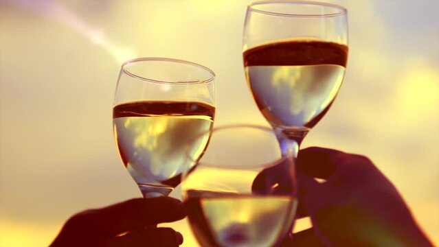 People holding Glass of Wine, Making a toast over Sunset sky. Birthday. Friends drinking White Wine, toasting. Clink. Party outdoors. Enjoying time together. Slow motion