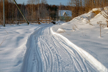 Obraz premium Village road with snowmobile tracks on a frosty winter day