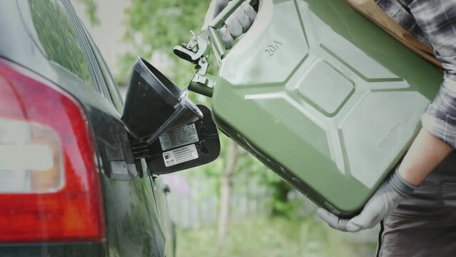Man pours gasoline from a green canister directly into the tank of a car. Green Jerrycan full of gas. Lack of fuel while traveling far. Close-up footage of gasoline flow in a slow motion