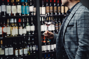 Concept choice of alcohol, hand of male sommelier in suit holds glass of red wine