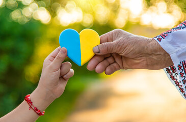 Grandmother holds in her hands a heart in the color of the Ukrainian flag. Selective focus.