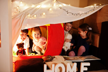 Fototapeta na wymiar Playing kids with kitty in tent at night home. Hygge mood.