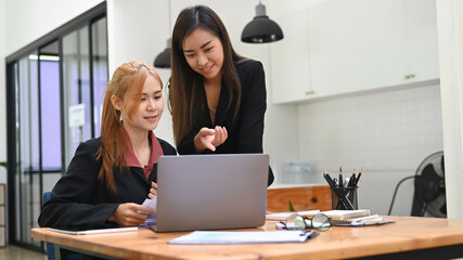 Asian female manager discussing online information with young employee in office