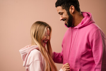 Romantic fashion studio portrait of a biracial young couple in love in hoodie posing over pink background.