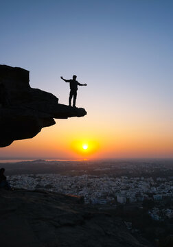 silhouette of a man standing on the edge of a cliff at sunset