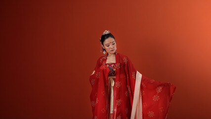 Young attractive Asian woman wearing tadeonal Chinese red hanfu long skirt dress costume scarf hairpin earring indoor on read marron background wall