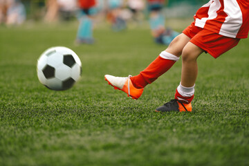 Soccer player kick ball on grass piitch. Football ball in motion. School soccer player in striped red and white uniform