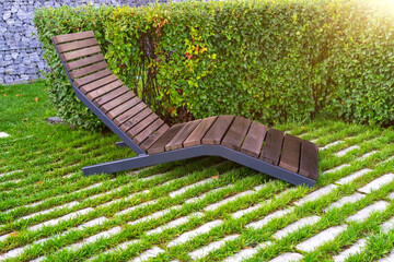 Alone empty brown wooden deck chair or chaise longue on tile and lawn among decorative bushes in...