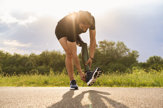 Disabled man athlete with leg prosthesis tying his shoes outdoors - ready for tryout